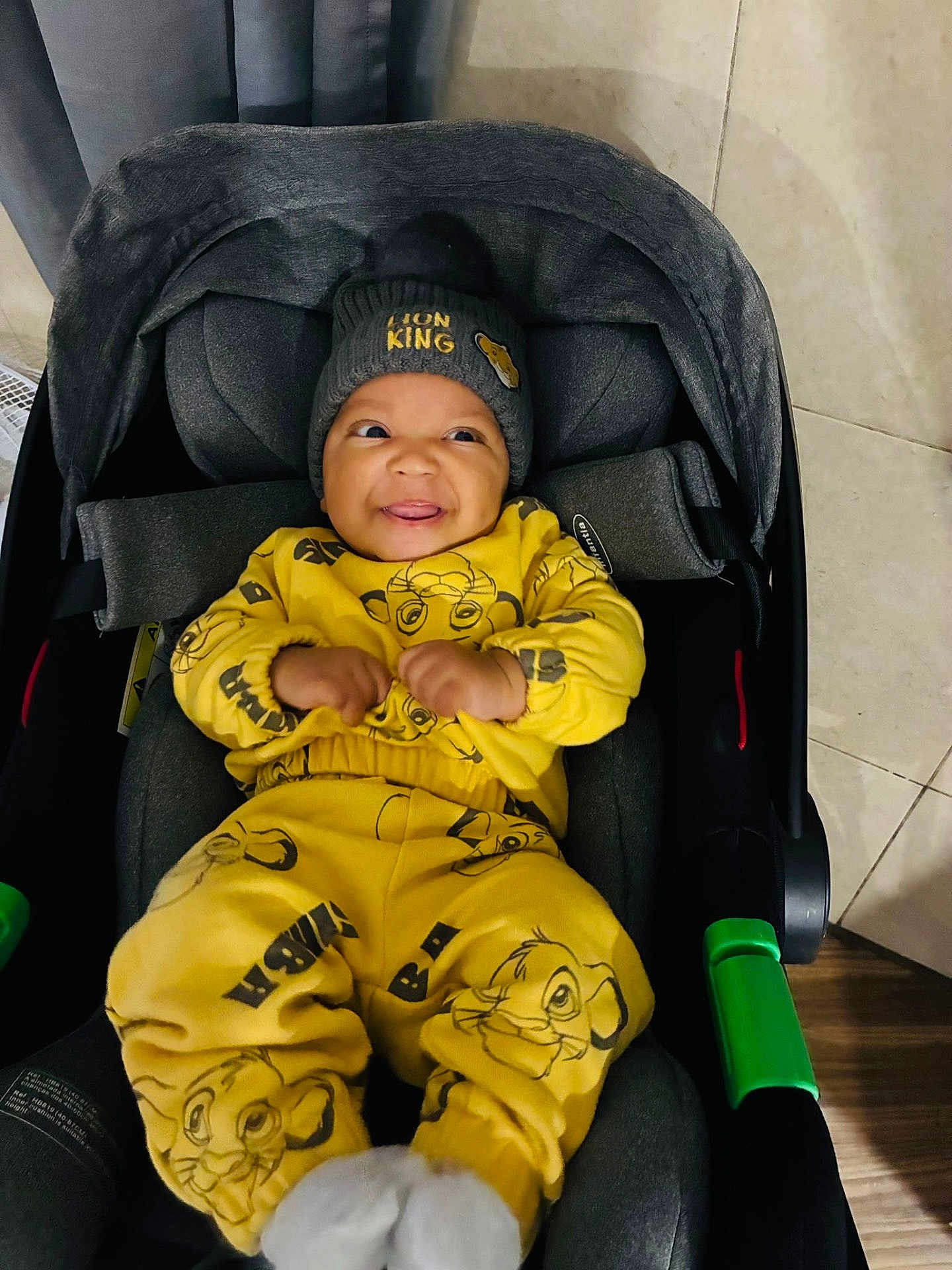 Ryan Tavares a rejoint le concours — aidez-le/la à gagner de superbes lots ! baby, child, smiling, yellow_clothing, lion_king, beanie, car_seat, indoor, happy, cute, infant, portrait, clothing, socks, floor, tile_floor, wood_floor, toy, seat_belt, fabric