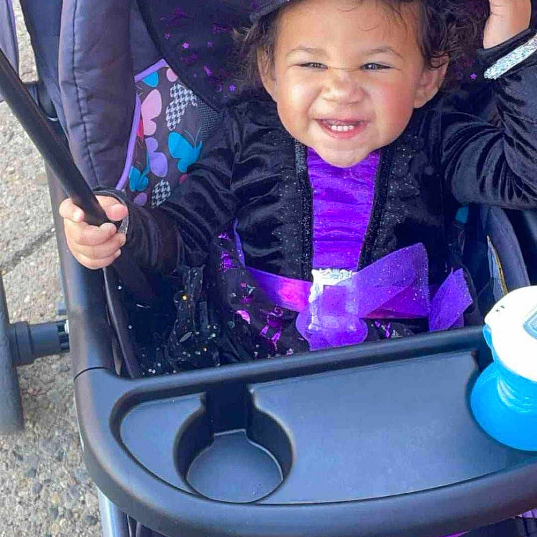 A'Rayah is registered to the contest to win money with this photo: baby, bodypart, carnival, clothing, coat, costume, face, happy, hat, head, jacket, mouth, outdoors, person, photography, portrait, purple, smile, stroller, teeth