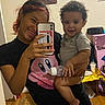 Jahkai joined the competition — help win amazing prizes! child, toddler, person, selfie, mirror_selfie, smiling, playful, tongue_out, curly_hair, indoor, home, portrait, holding_child, phone, smartphone, pink_phone_case, toy, table, wooden_floor, casual_clothing