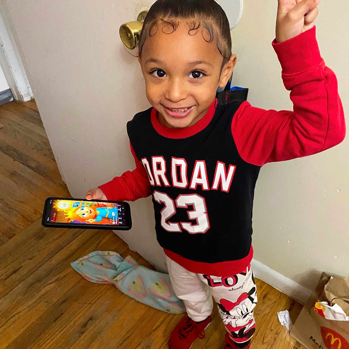 Iyasia joined the competition — help win amazing prizes! child, toddler, smiling, portrait, indoor, standing, victory_sign, red_clothing, sporty_outfit, phone, smartphone, hair_bun, face, wooden_floor, door, blanket, minnie_mouse, sneakers, fast_food, mcdonalds