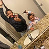 child, girl, sibling, selfie, mirror, bathroom, smiling, playful, funny_face, braid, hair, jacket, pajamas, toy, countertop, granite, sink, faucet, soap_bottle, portrait