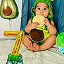 baby, infant, avocado_costume, balloon, number_balloon, milestone_plaque, carpet, blue_curtain, cute, child, celebration, smiling, sitting, plush_toy, foot, hand, indoor, photo, birthday, party_decoration