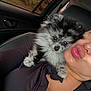puppy, dog, person, car_interior, window, seat, black_clothing, fur, cute, pet, face, portrait, travel, shoulder, kiss, expression, animal, closeup, indoor, leisure
