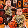 children, toddlers, basketball, sports, basketball_court, indoor, portrait, smiling, standing, sitting, athletic, sportswear, jerseys, sneakers, basketballs, basketball_hoop, gymnasium, wooden_floor, siblings, playful