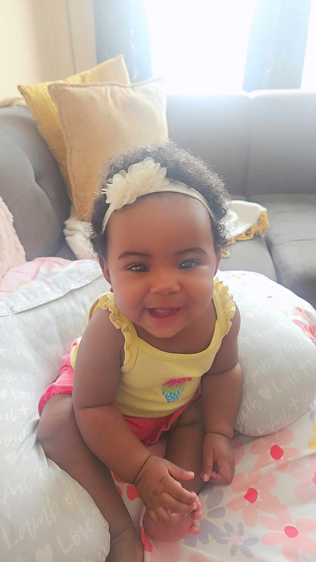 Madison joined the competition — help win amazing prizes! baby, child, smiling, headband, flower, cushion, pillow, sofa, living_room, cute, happy, sitting, indoors, skin, clothing, yellow_top, pink_shorts, infant, portrait, cozy