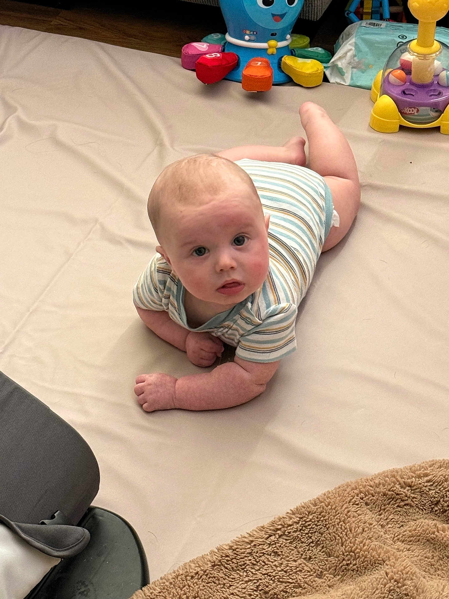 Casen joined the competition — help win amazing prizes! baby, infant, tummy_time, onesie, playmat, toy, colorful_toys, blanket, diaper, indoor, curious, lying_down, portrait, face, hands, floor, play_area, soft_toy, wooden_floor, living_room