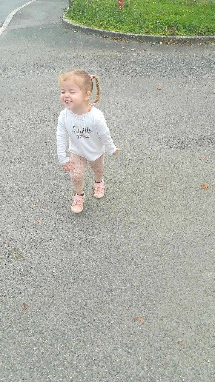 Zélya participe au concours pour gagner de l'argent avec cette photo : toddler, child, outdoor, pavement, grass, curb, sidewalk, happy, walking, shoes, braids, long_sleeve_shirt, pants, smiling, young_child, daylight, casual_clothing, nature, playful, person