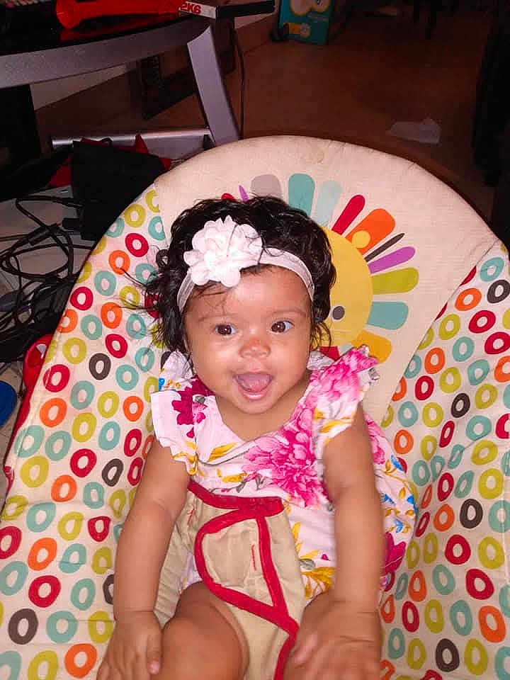 Mersada is registered to the contest to win money with this photo: baby, child, smiling, flower_headband, floral_dress, colorful, baby_chair, patterned, indoor, happy, cute, sitting, infant, young_child, person, headband, dress, face, skin, hair