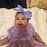 Sarah joined the competition — help win amazing prizes! baby, child, smiling, purple_dress, headband, bow, blanket, patterned_pillow, happy, cute, face, portrait, infant, sitting, clothing, fabric, indoor, person, flower_pattern, accessory