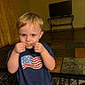 american_flag, boy, carpet, child, curtains, cute, expression, furniture, holding, home, indoor, living_room, person, portrait, shirt, shorts, table, tape, television, toddler