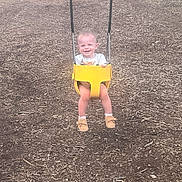 Kadence is registered to the contest to win money with this photo: child, toddler, swing, playground, yellow_swing, smiling, happy, outdoor, wood_chips, baby_shoes, white_socks, shorts, tshirt, play, fun, joy, person, seat, metal_chains, nature