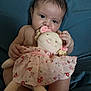 baby, child, plush_doll, soft_toy, pink_dress, floral_pattern, sitting, curious, indoor, cute, face, hands, legs, skin, head, expression, comfort, background, nurture, infant