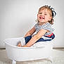 toddler, child, smiling, striped_clothing, beret, white_tub, clawfoot_tub, curly_hair, happy, sitting, portrait, studio, white_background, floor_rug, cute, playful, cheerful, indoor, person, baby