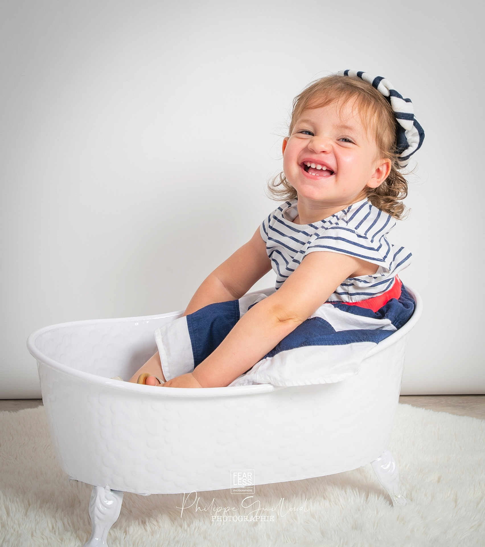 Sybille participe au concours pour gagner de l'argent avec cette photo : toddler, child, smiling, striped_clothing, beret, white_tub, clawfoot_tub, curly_hair, happy, sitting, portrait, studio, white_background, floor_rug, cute, playful, cheerful, indoor, person, baby