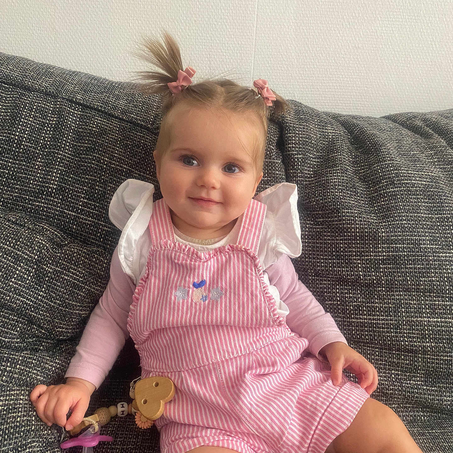 Iris a rejoint le concours — aidez-le/la à gagner de superbes lots ! baby, child, couch, cute, face, furniture, hair, hand, indoors, long_sleeve_shirt, pacifier, pigtails, pink_bows, portrait, sitting, smile, striped_romper, textured_fabric, toddler, wooden_heart