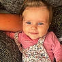 baby, child, smiling, blue_eyes, ponytail, pink_shirt, floral_overall, cushion, blanket, cozy, indoor, portrait, cute, infant, happy, closeup, person, soft_lighting, relaxed, home