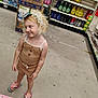 aisle, blonde_hair, casual_wear, child, clothing, cute, flip_flops, floor, footwear, headwear, household_products, indoor, person, product_boxes, shelves, shopping, smile, store, tinsel, young_child