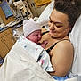 newborn, baby, mother, hospital, blanket, bed, medical_equipment, cap, woman, infant, love, care, gaze, indoor, healthcare, patient, tenderness, family, postpartum, portrait