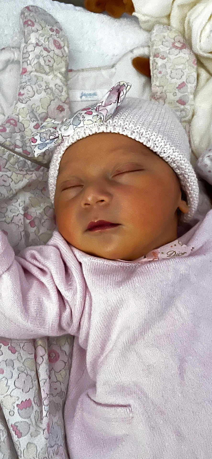 Maria a rejoint le concours — aidez-le/la à gagner de superbes lots ! baby, sleeping, infant, knit_hat, bow, pink_clothing, blanket, floral_pattern, closeup, face, peaceful, cute, soft_texture, newborn, child, portrait, resting, indoors, cozy, warm