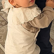 Maria participe au concours pour gagner de l'argent avec cette photo : baby, beige, child, clothing, coat, curious, cute, earrings, floor, girl, hair_bow, holding_leg, indoor, looking_back, patterned_floor, person, portrait, small, toddler, white