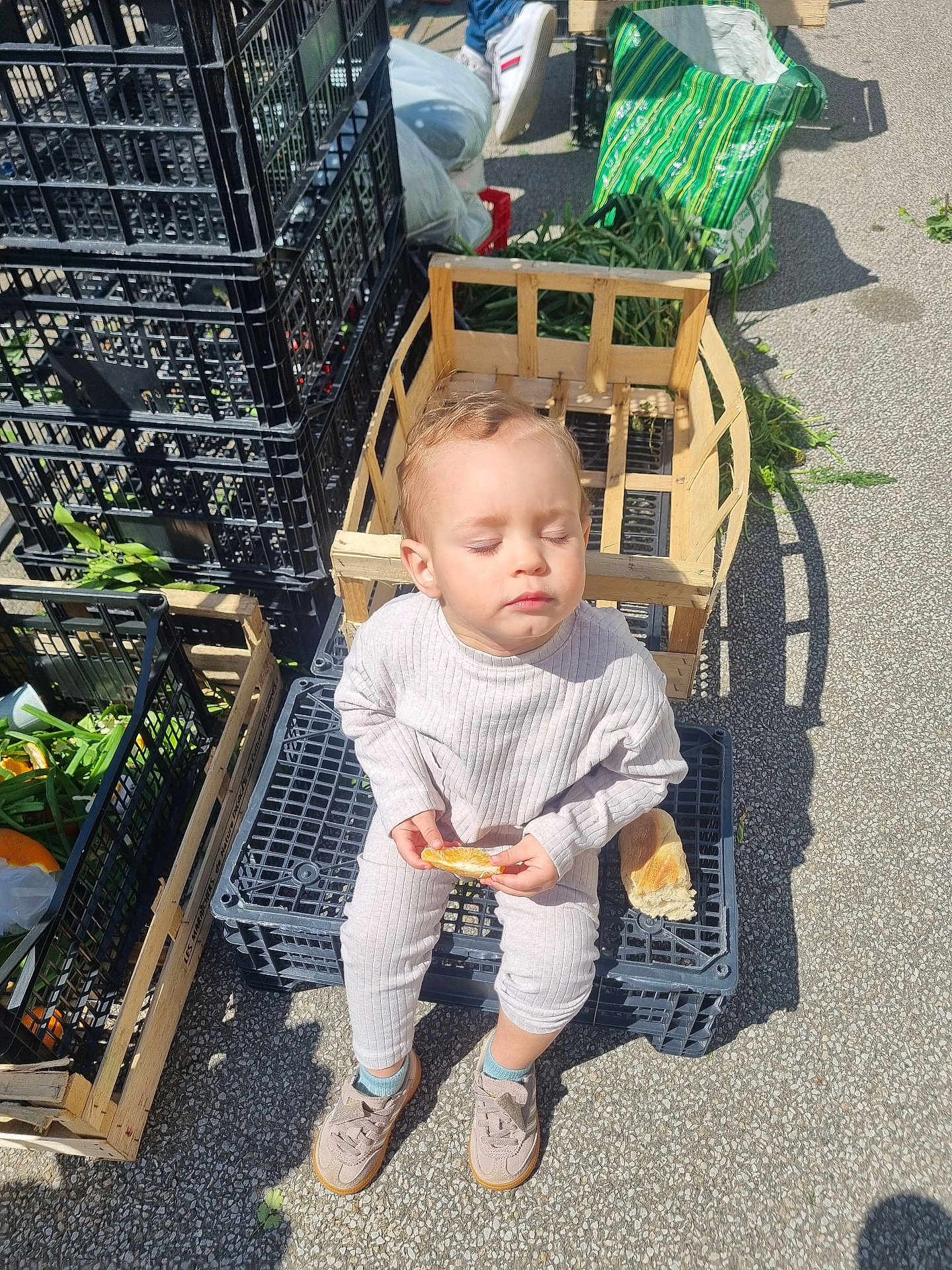 Zayn participe au concours pour gagner de l'argent avec cette photo : toddler, child, sitting, bread, baguette, crate, vegetables, outdoor, sunlight, closed_eyes, shoes, clothing, asphalt, plastic_crate, bag, greenery, person, food, market, peaceful
