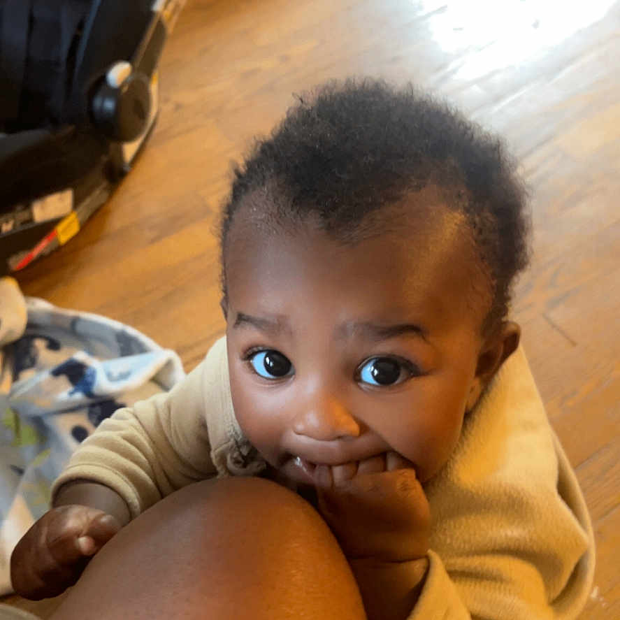 Hazion is registered to the contest to win money with this photo: baby, blanket, bright_eyes, car_seat, child, curious, cute, face, floor, hand, indoor, infant, knee, person, playing, skin, smiling, wearing_clothes, wooden_floor, young