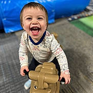 Deklan is registered to the contest to win money with this photo: carpet, child, clothing, colorful, cute, face, floor, fun, happy, indoor, joy, person, plastic_toy, play, playground, riding, smiling, toddler, toy, young_child