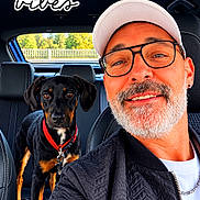 Murphy participe au concours pour gagner de l'argent avec cette photo : man, person, dog, black_dog, tan_markings, car, car_interior, selfie, portrait, glasses, hat, beard, smiling, red_collar, leash, seated, outdoor, sunlight, good_vibes, music_overlay