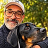 Murphy a rejoint le concours — aidez-le/la à gagner de superbes lots ! man, dog, doberman, pet, owner, selfie, portrait, outdoors, forest, woodland, bokeh, sunlight, smiling, glasses, baseball_cap, beard, black_dog, tan_markings, red_harness, cuddling