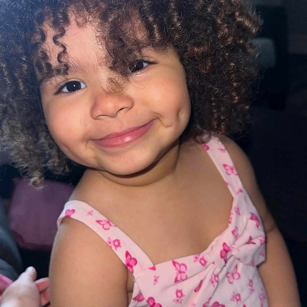 Ayla is registered to the contest to win money with this photo: butterfly_pattern, child, childhood, clothing, curly_hair, cute, dimples, face, fashion, female, hand, happy, indoor, person, pink_dress, portrait, skin, smile, toddler, young