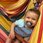 Martin a rejoint le concours — aidez-le/la à gagner de superbes lots ! baby, pacifier, hammock, striped, colorful, child, smiling, clothing, shorts, tshirt, wooden_stick, relaxing, outdoor, happy, cute, infant, legs, hand, face, portrait