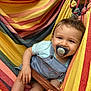 baby, pacifier, hammock, striped, colorful, child, smiling, clothing, shorts, tshirt, wooden_stick, relaxing, outdoor, happy, cute, infant, legs, hand, face, portrait