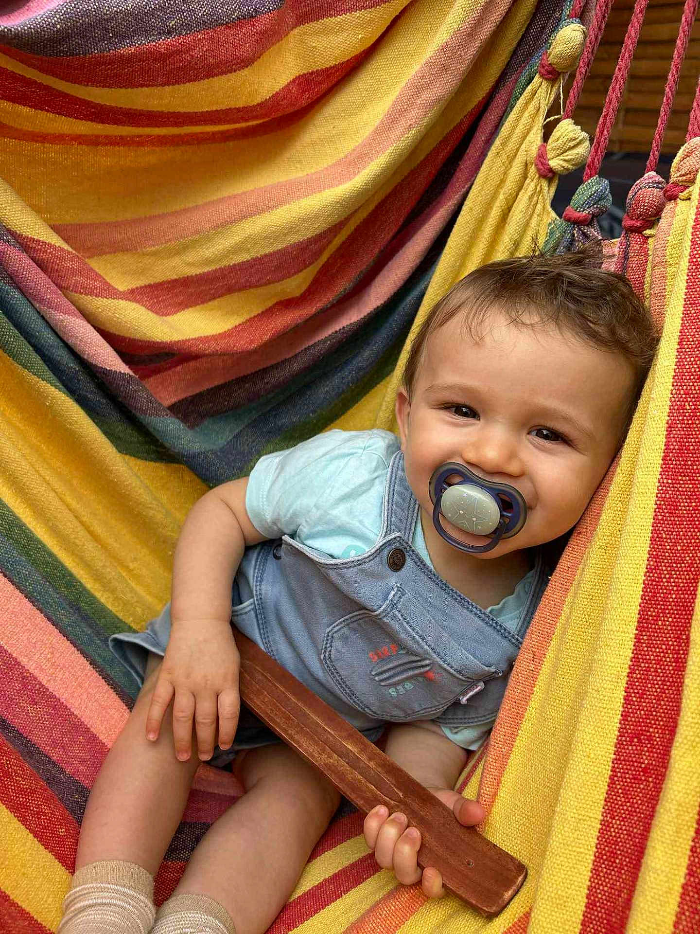 Martin a rejoint le concours — aidez-le/la à gagner de superbes lots ! baby, pacifier, hammock, striped, colorful, child, smiling, clothing, shorts, tshirt, wooden_stick, relaxing, outdoor, happy, cute, infant, legs, hand, face, portrait