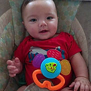 Shauann is registered to the contest to win money with this photo: baby, infant, child, toy, red_shirt, cushion, seat, smile, hand, face, colorful, bee, cute, indoor, person, small_hands, plush, happy, young, portrait