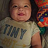 baby, infant, smiling, tshirt, text, toy, colorful, pattern, lying_down, face, cute, child, playful, indoors, soft, fabric, person, skin, head, arm