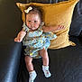 Nova is registered to the contest to win money with this photo: baby, infant, child, couch, leather, pillow, yellow_pillow, black_couch, dress, floral_dress, socks, white_socks, hair_bow, indoor, furniture, person, skin, cute, seated, looking