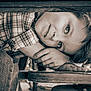 child, face, hands, wood, table, plaid_shirt, sepia, portrait, resting, young, curly_hair, furniture, casual_clothing, close_up, thoughtful, indoor, relaxed, natural_light, person, expression