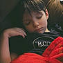 child, sleeping, blanket, couch, red_blanket, black_shirt, relaxation, indoors, peaceful, rest, young, face, hand, hair, casual_clothing, portrait, cozy, comfort, nap, home