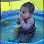 baby, infant, pool, water, toy, swimsuit, leopard_print, sitting, child, playtime, inflatable_pool, yellow_canopy, chewing, cute, summer, outdoor, floating_toys, chubby, water_play, heart_doodle