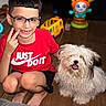 King joined the competition — help win amazing prizes! child, boy, glasses, red_shirt, peace_sign, dog, fluffy_dog, indoor, toy, floor, smiling, happy, short_hair, barefoot, pet, cute, playful, person, casual_clothing, home