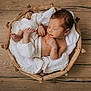 newborn, baby, sleeping, infant, basket, wooden_basket, white_clothing, knitted, cozy, blanket, wood_floor, peaceful, cute, child, portrait, indoors, resting, small, soft, wrapped