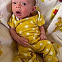baby, infant, yellow_clothing, sun_pattern, blanket, giraffe_print, soft_fabric, surprised_expression, sitting, newborn, cute, child, person, indoors, cozy, comfort, portrait, small_hands, barefoot, head
