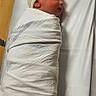 Ronald is registered to the contest to win money with this photo: newborn, baby, hospital, blanket, bassinet, wrapped, infant, cap, bed, sleeping, side_view, cute, small, person, child, indoors, healthcare, resting, soft_light, cozy