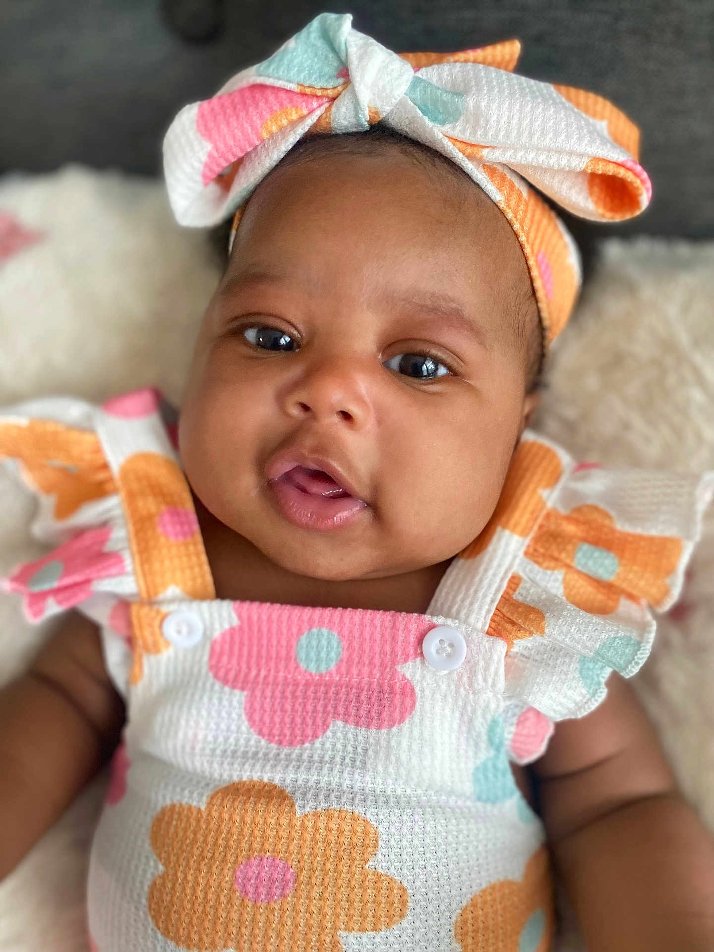 Xamira is registered to the contest to win money with this photo: baby, infant, child, face, headband, bow, clothing, floral_pattern, cute, portrait, skin, eyes, mouth, soft_texture, fabric, sleeveless, colorful, pink, orange, white
