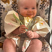 Bonnie is registered to the contest to win money with this photo: baby, child, high_chair, spoon, messy_face, smiling, food, feeding, infant, cute, playful_background, cartoon_animals, floral_pattern, clothing, sitting, happy, portrait, indoors, person, mealtime