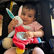 Lilia a rejoint le concours — aidez-le/la à gagner de superbes lots ! baby, child, smiling, plush_toy, bunny, stroller, seatbelt, pink_clothing, happy, cute, indoor, person, infant, soft_toy, toddler, playful, comfort, closeup, portrait, cuddly