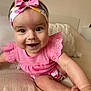 baby, child, smiling, pink_clothing, headband, bow, couch, cushion, indoor, happy, cute, infant, person, portrait, sitting, closeup, face, skin, hand, foot