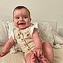 baby, smiling, infant, couch, pillow, clothing, romper, barefoot, hand, foot, cute, indoors, child, person, happy, sitting, skin, furniture, texture, light