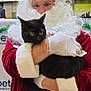 santa_claus, black_cat, costume, glasses, white_beard, white_gloves, red_clothing, indoor, holiday, christmas, decorations, person, animal, pet, holding, fur, festive, portrait, cute, wide_eyes