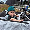Vincent joined the competition — help win amazing prizes! baby, child, infant, toddler, portrait, outdoor, park, wagon, stroller, backward_cap, teal_clothing, black_shirt, serious_expression, face, eyes, hands, fence, grass, trees, cup_holder